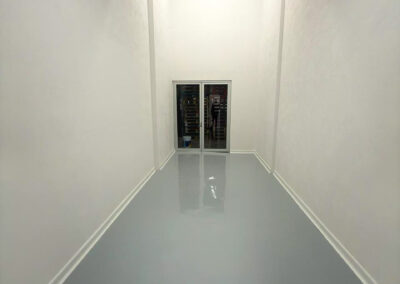 Long white room with a white cove base along a gray floor and a glass door at the end